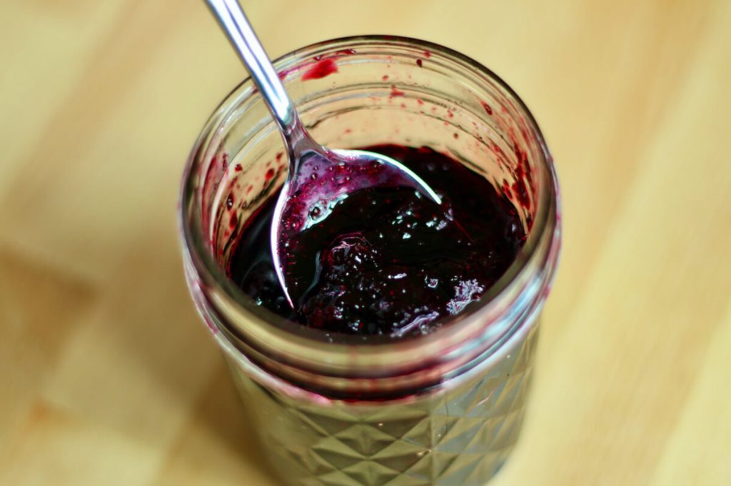 An open jar of blueberry jam with a spoon sitting inside the jar.