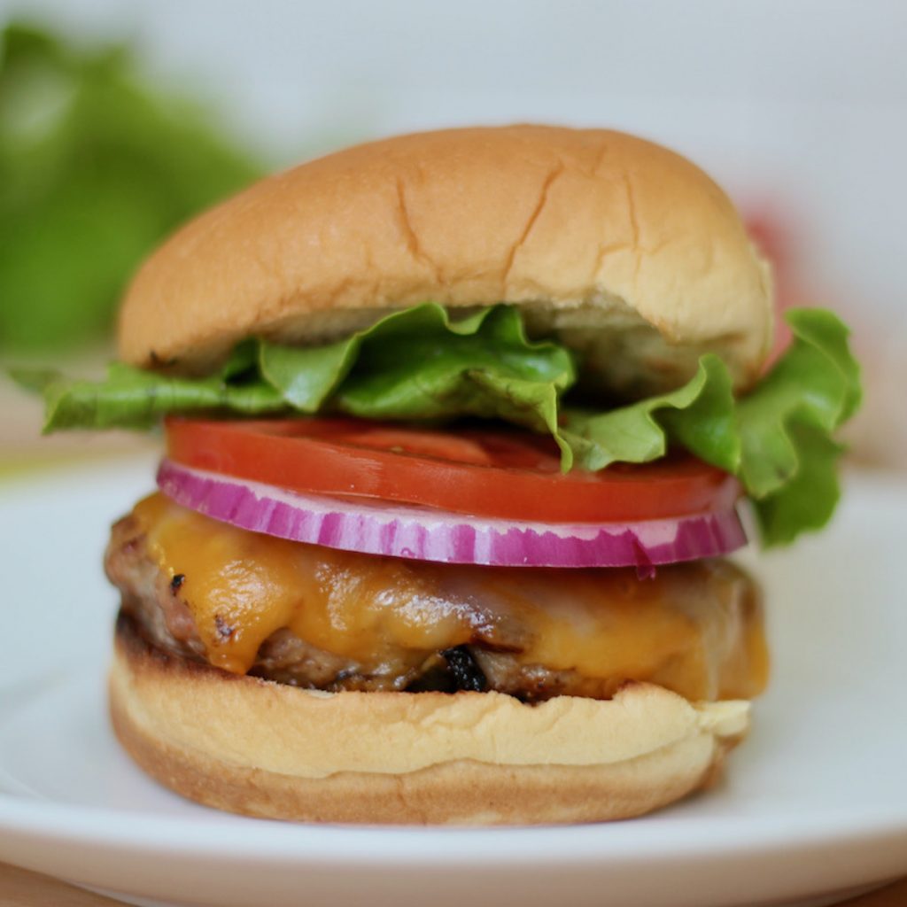 A turkey smash burger topped with red onion, tomato, and lettuce on a potato bun.