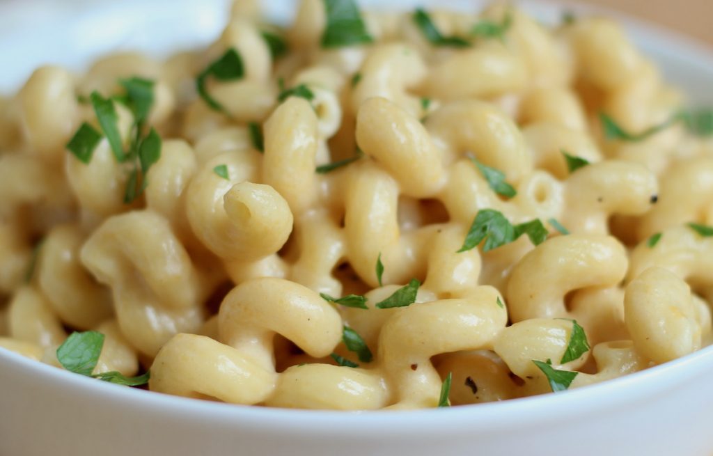 A white bowl filled with dutch oven mac and cheese. The pasta is garnished with fresh parsley.