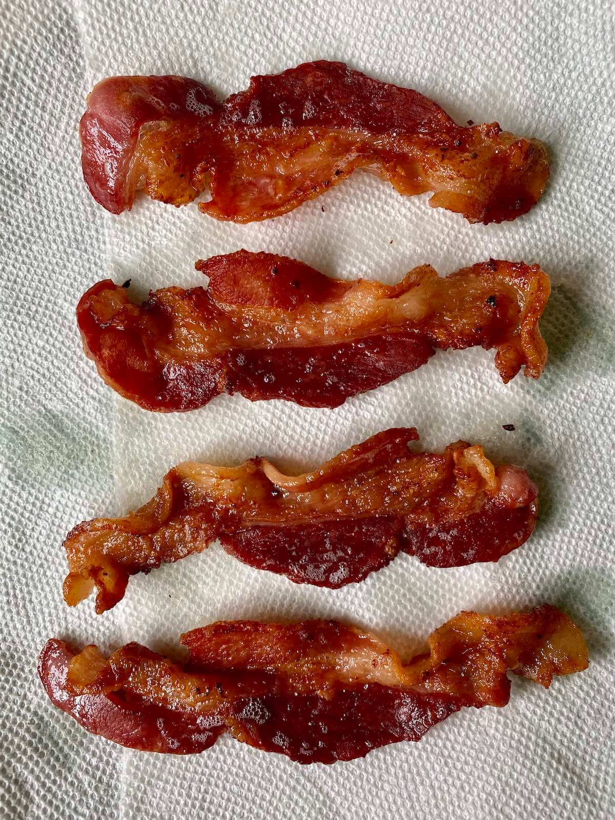 Four cooked strips of bacon draining on a paper towel.
