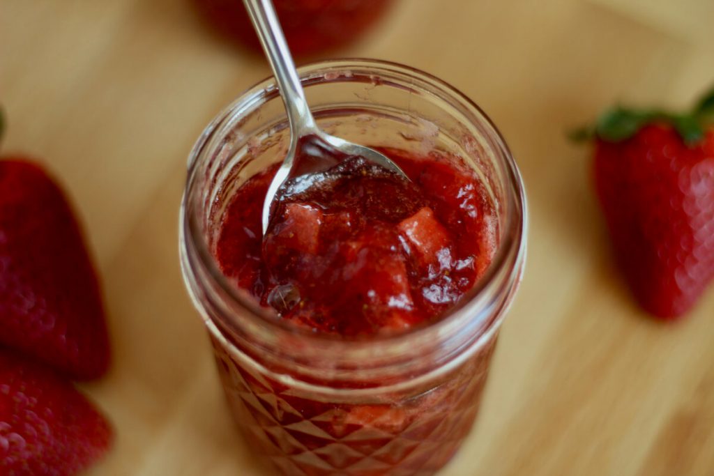an open jar of strawberry apple jam with a spoon inside