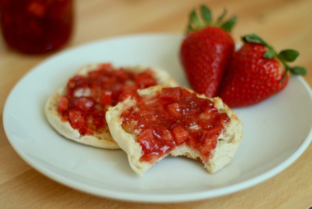 an english muffin topped with strawberry apple jam and butter with a bite taken out of it