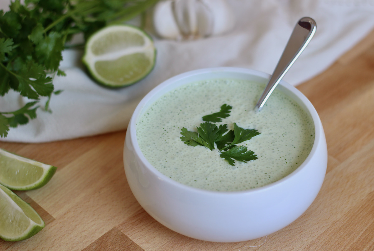 A white bowl of cilantro garlic sauce sitting on a butcher block countertop. The sauce is garnished with cilantro.