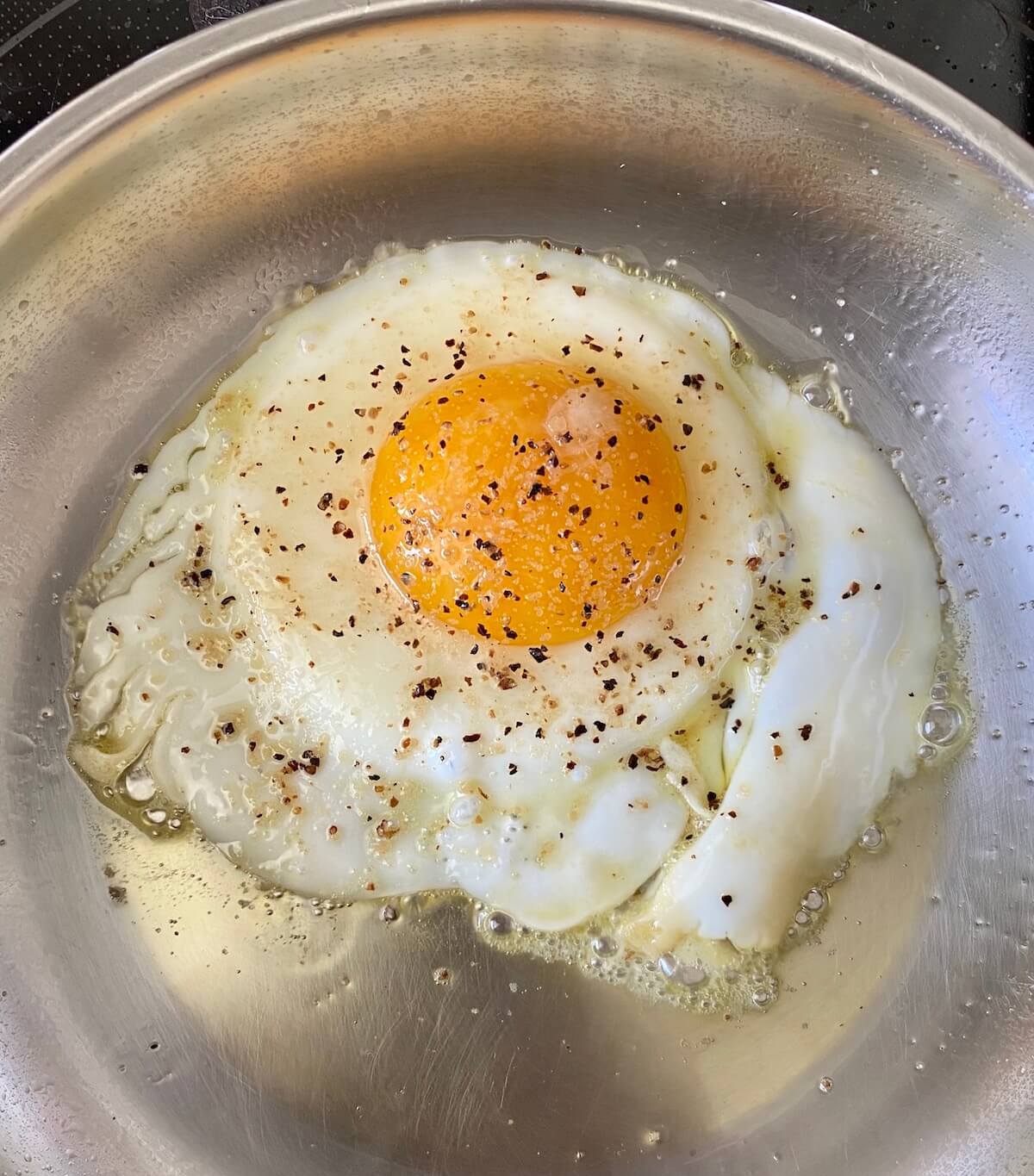An egg frying in a pan on the stove top.