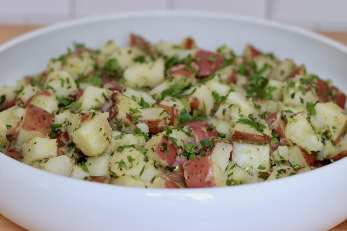 A large, shallow white dish filled with herbed potato salad.