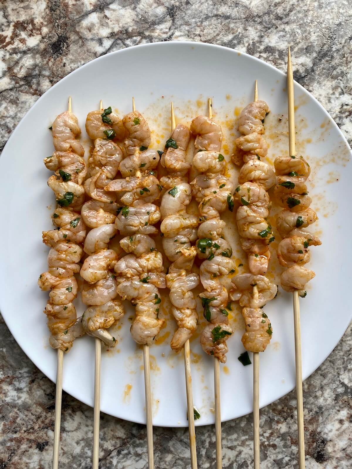 Raw, marinated shrimp on bamboo skewers on a white plate.