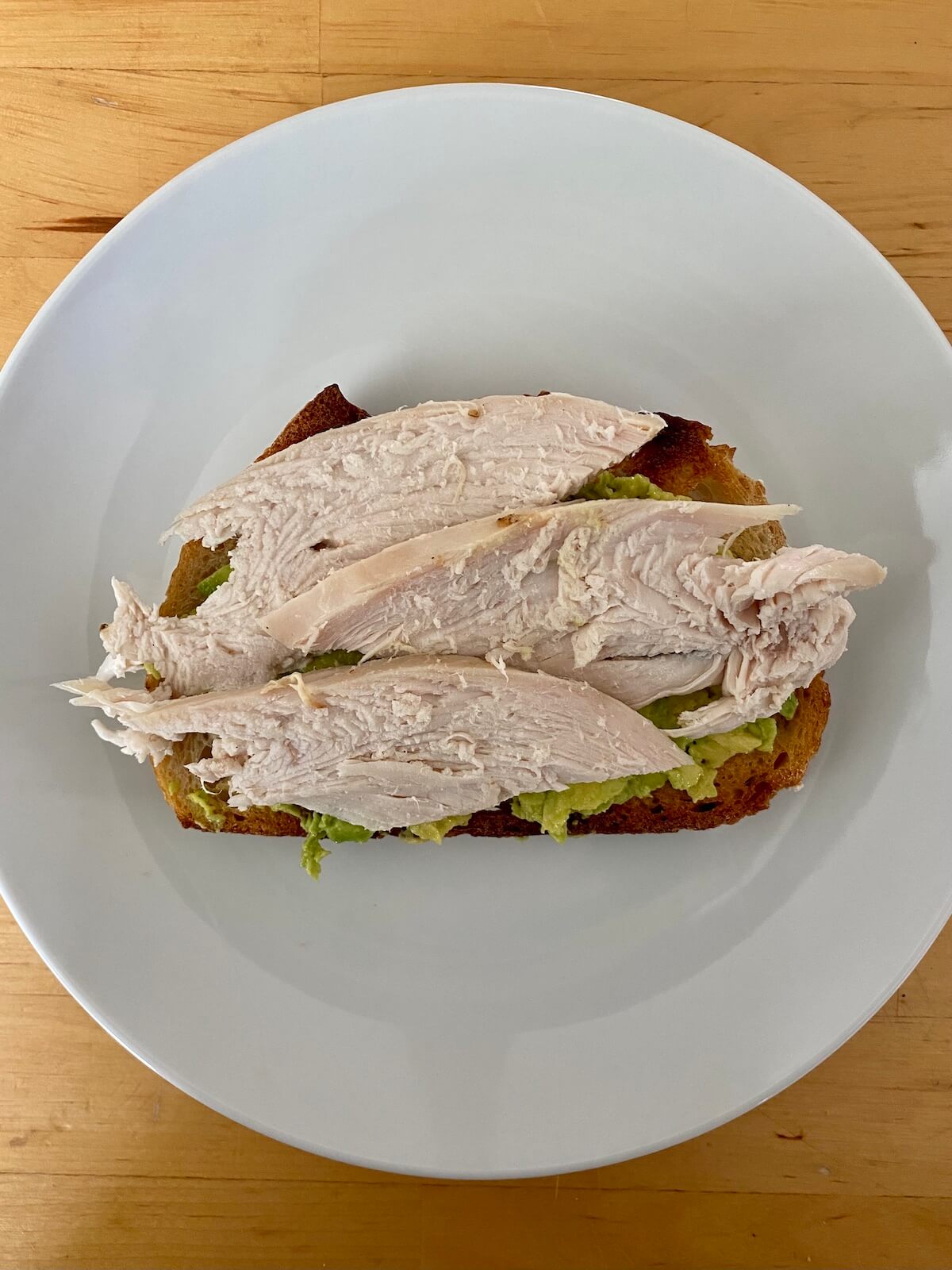 Mashed avocado and sliced roasted turkey breast on a piece of toasted sourdough bread.