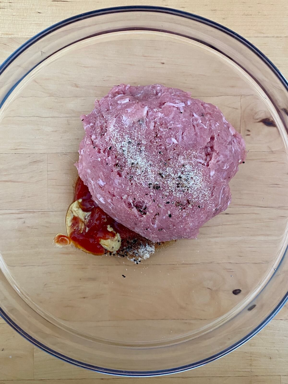 Ground turkey, ketchup, mustard, soy sauce, and other seasonings in a glass bowl.