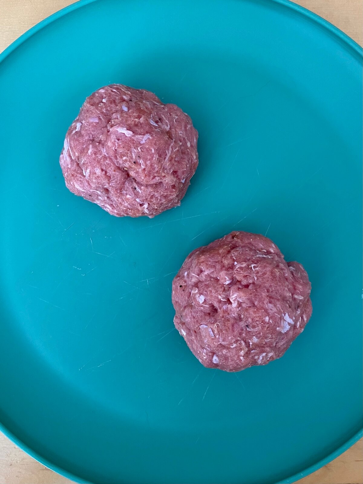 Two formed turkey burger balls on a green plate.