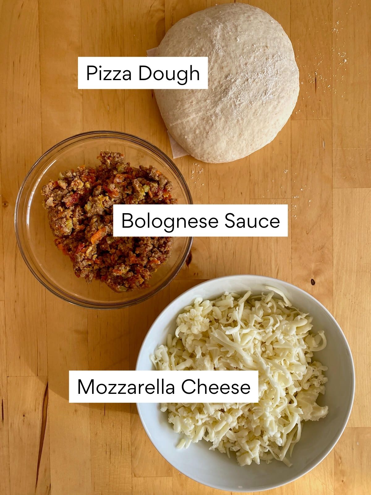 The ingredients to make bolognese pizza. Each ingredient is labeled with text. They include pizza dough, bolognese sauce, and mozzarella cheese.