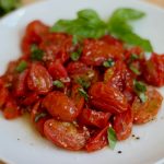 Roasted air fryer tomatoes garnished with fresh basil on a white plate.