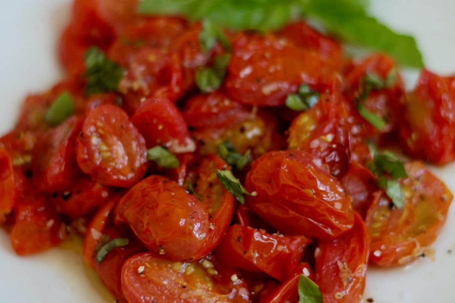 Roasted air fryer tomatoes garnished with fresh basil on a white plate.