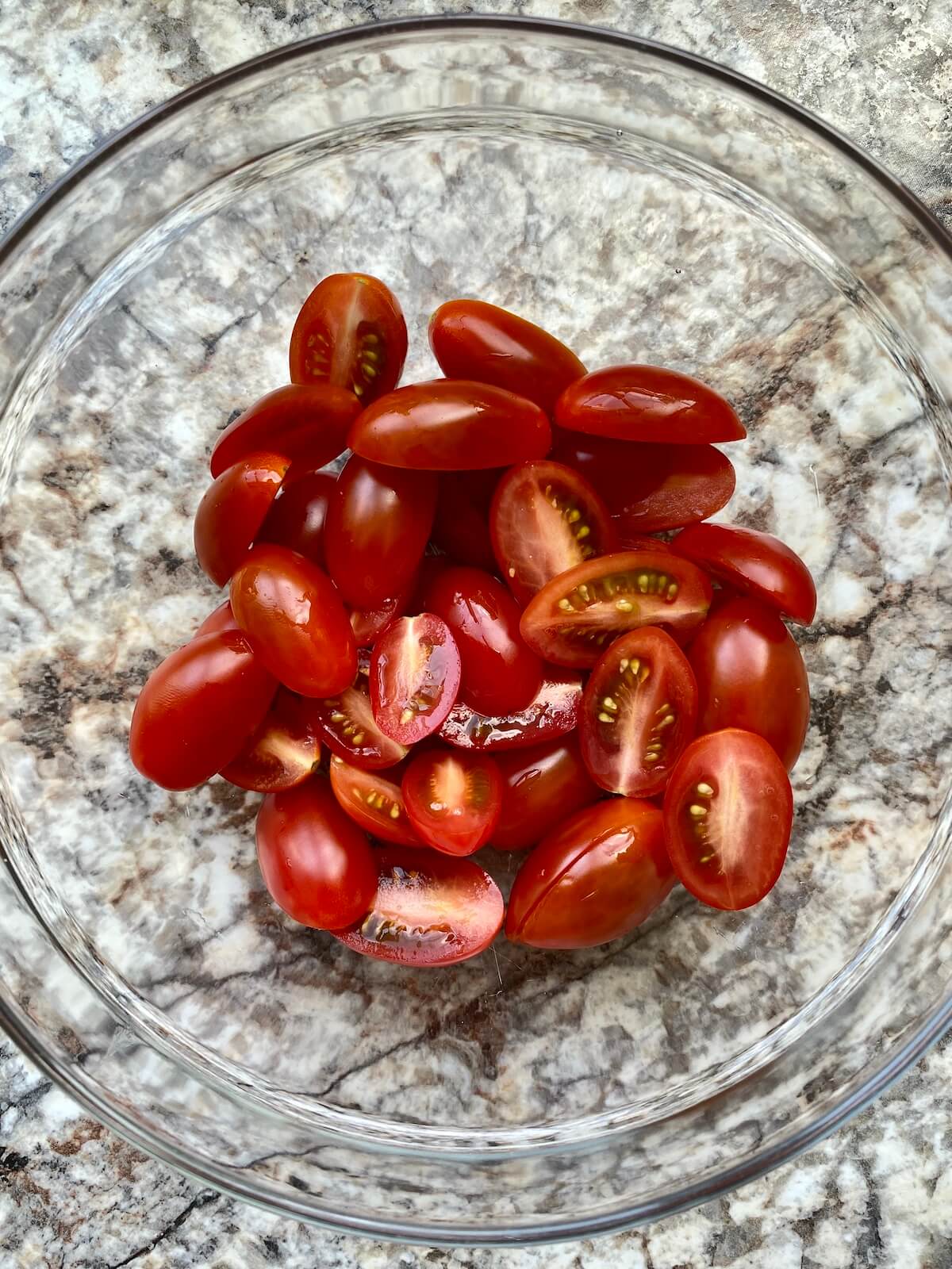 A clear glass bowl filled with rinsed and halved cherry tomatoes.