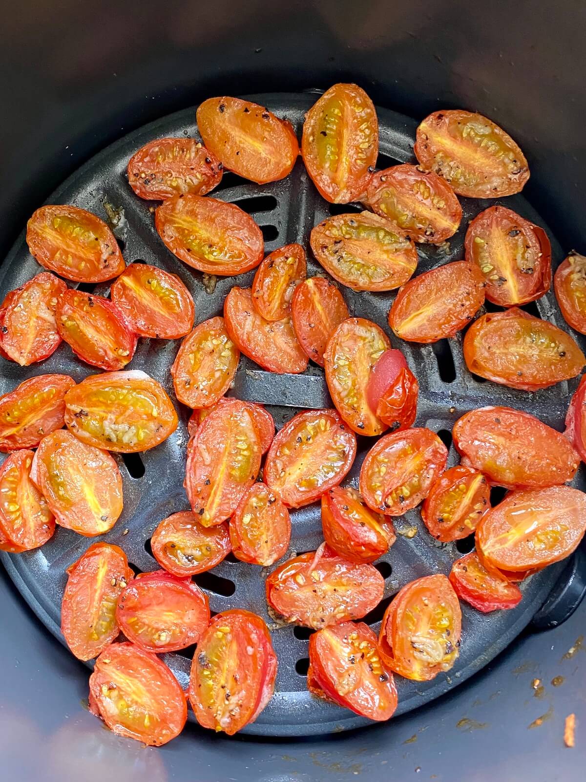 An air fryer basket with finished roasted cherry tomatoes inside.