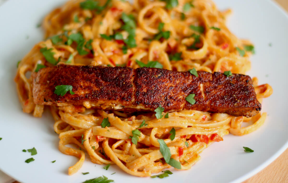 A fillet of blackened salmon sitting on a bed of creamy Cajun alfredo pasta and garnished with fresh parsley.