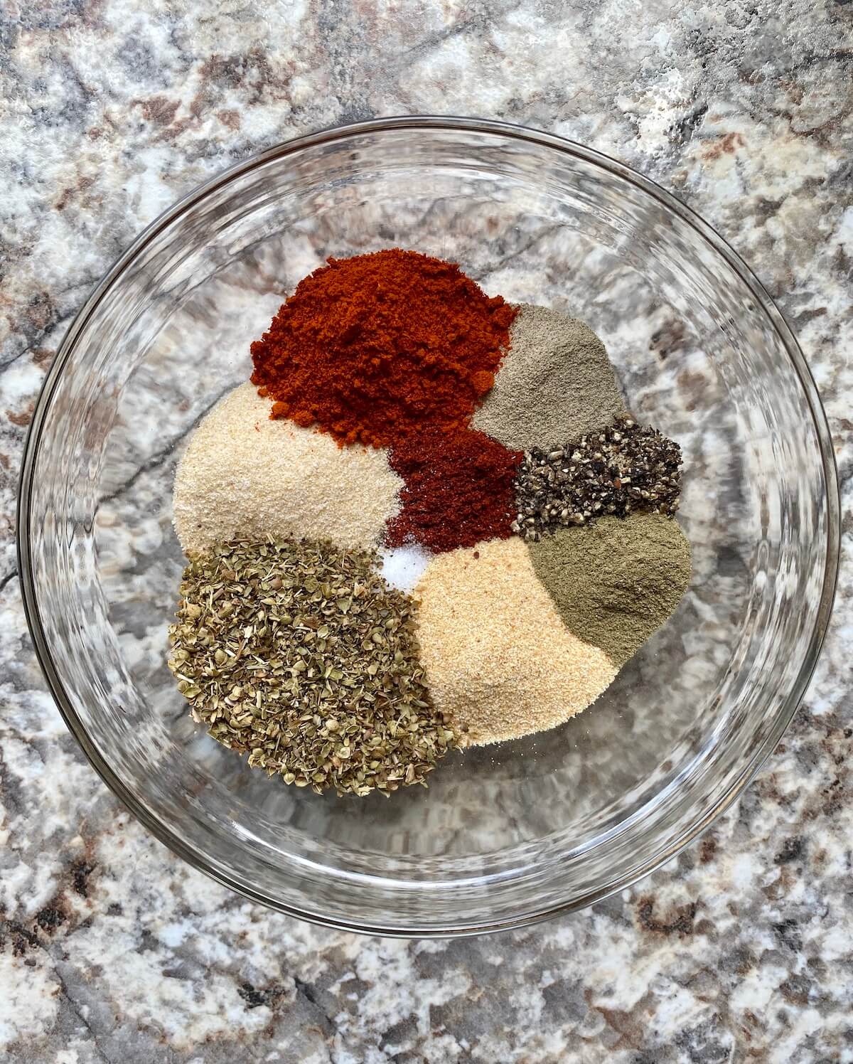 A small, clear glass bowl filled with the spices that make up Cajun seasoning. The spices have not yet been mixed together.