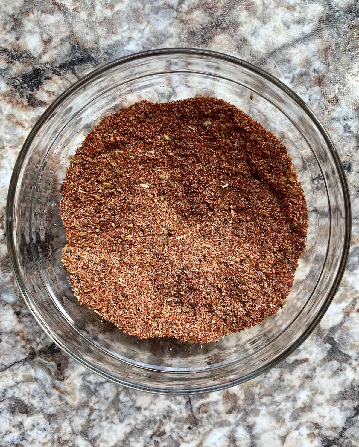 A small, clear glass bowl filled with Cajun seasoning after it has all be mixed together.