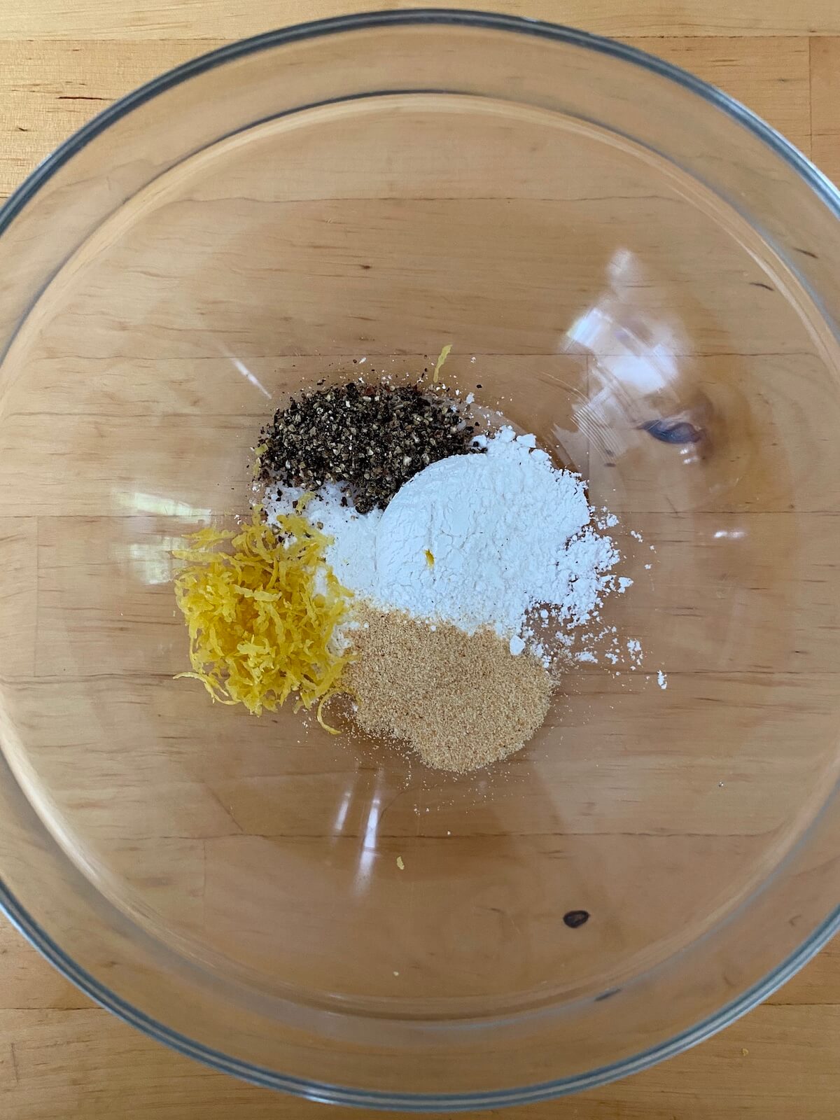 A small glass bowl with baking powder, lemon zest, garlic powder, black pepper, and salt inside of it.
