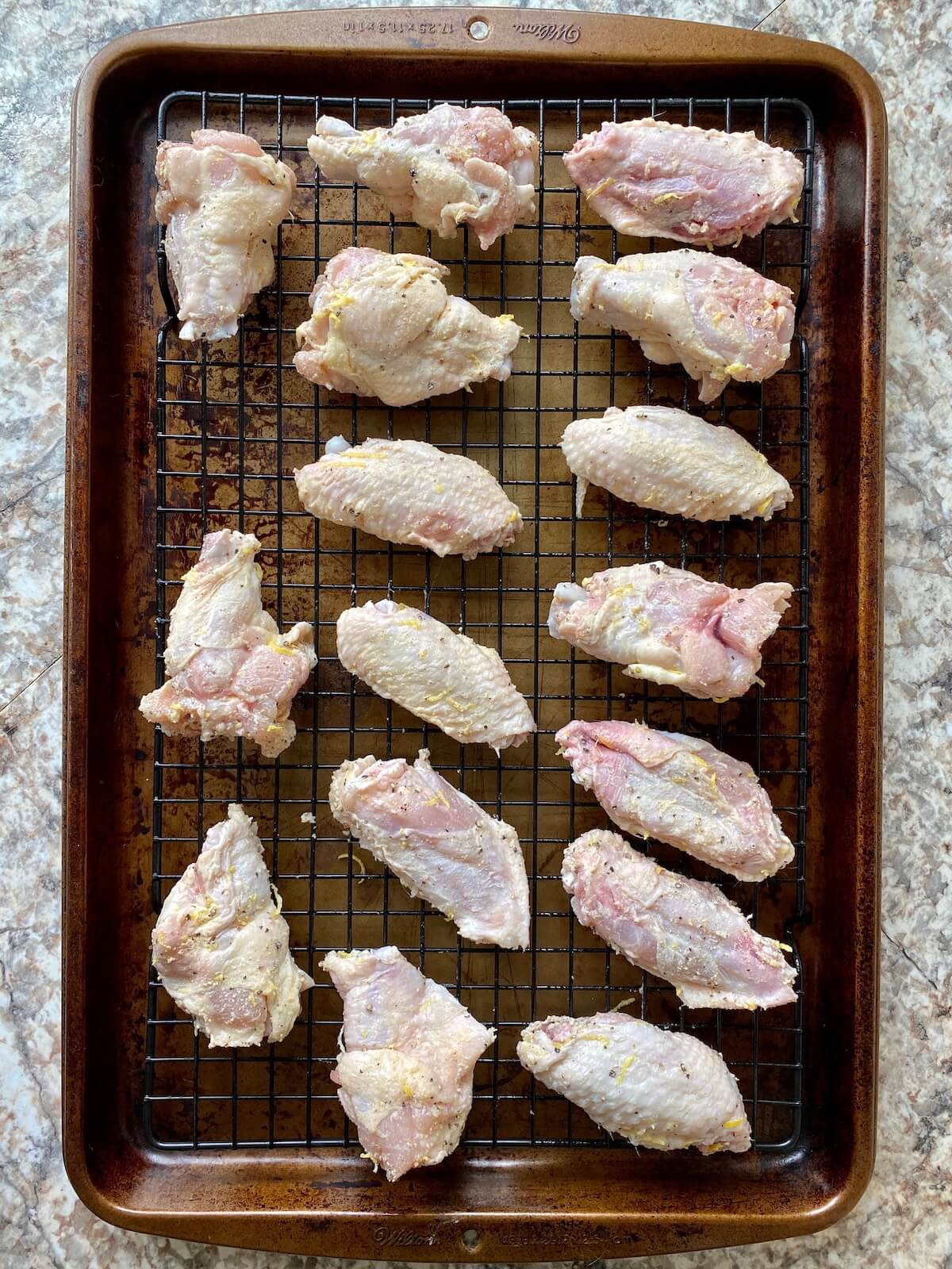 Raw chicken wings coated in baking powder and seasonings placed in a single layer on a wire rack on top of a baking sheet.