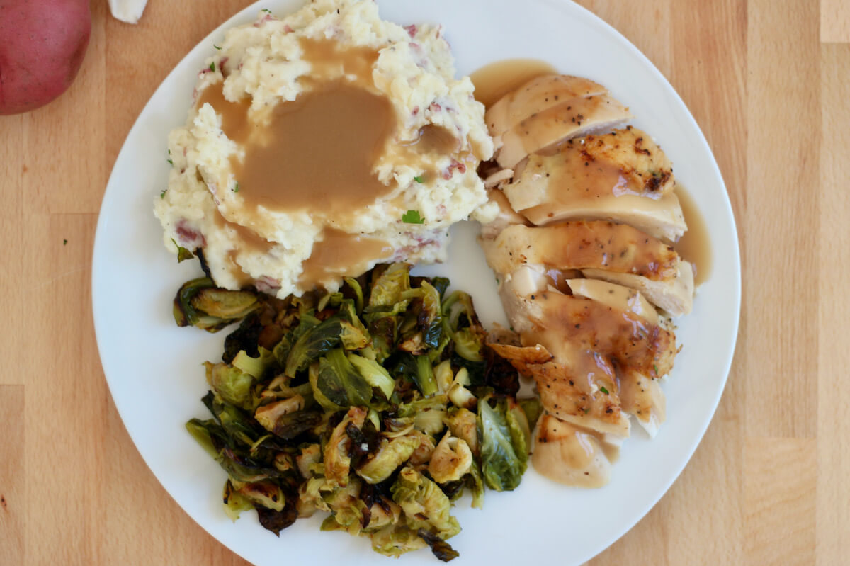 Garlic mashed red skin potatoes with roasted chicken, Brussels sprouts, and gravy on a white plate.