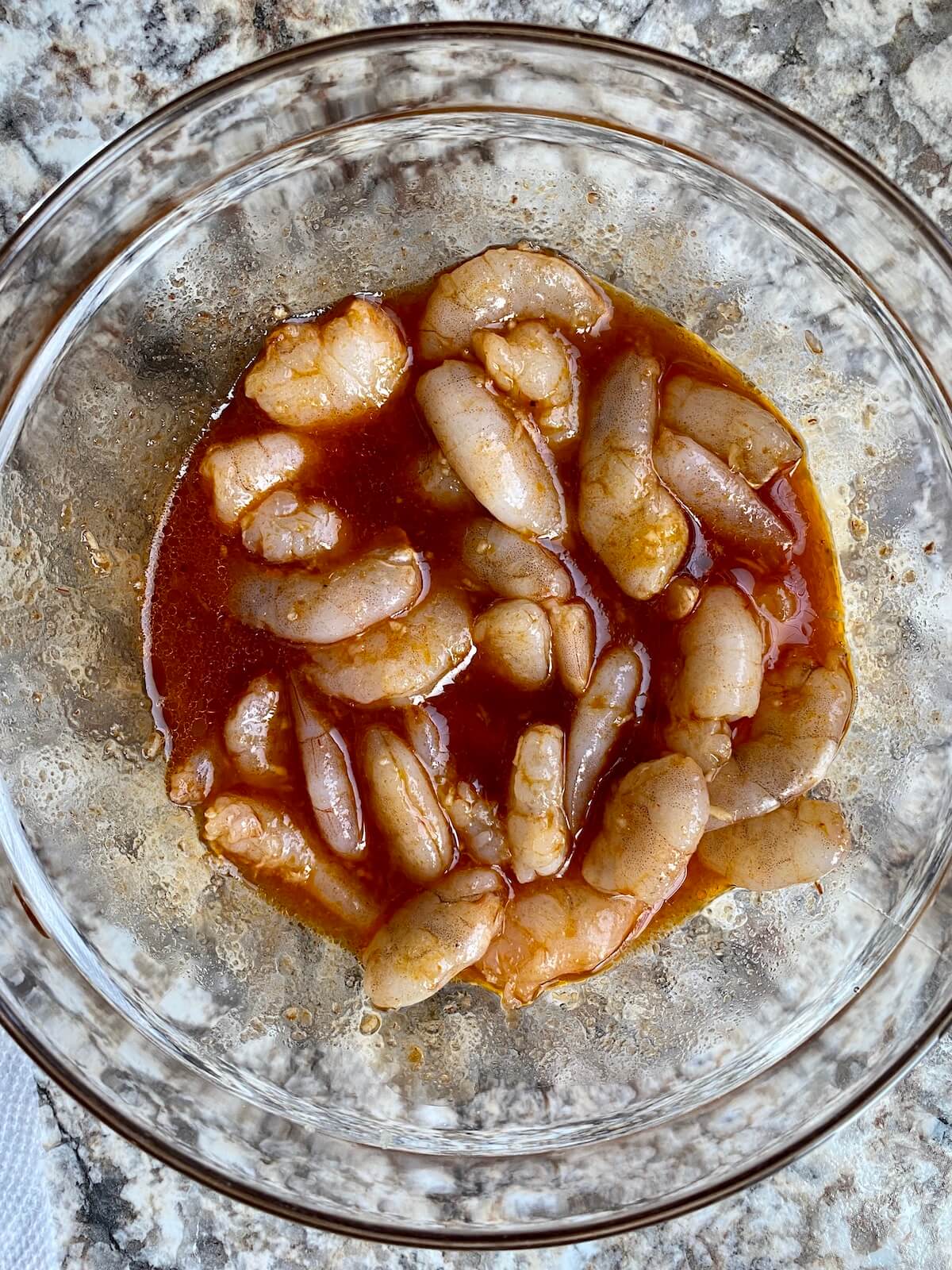 A clear bowl that contains raw shrimp marinating in honey chipotle marinade.