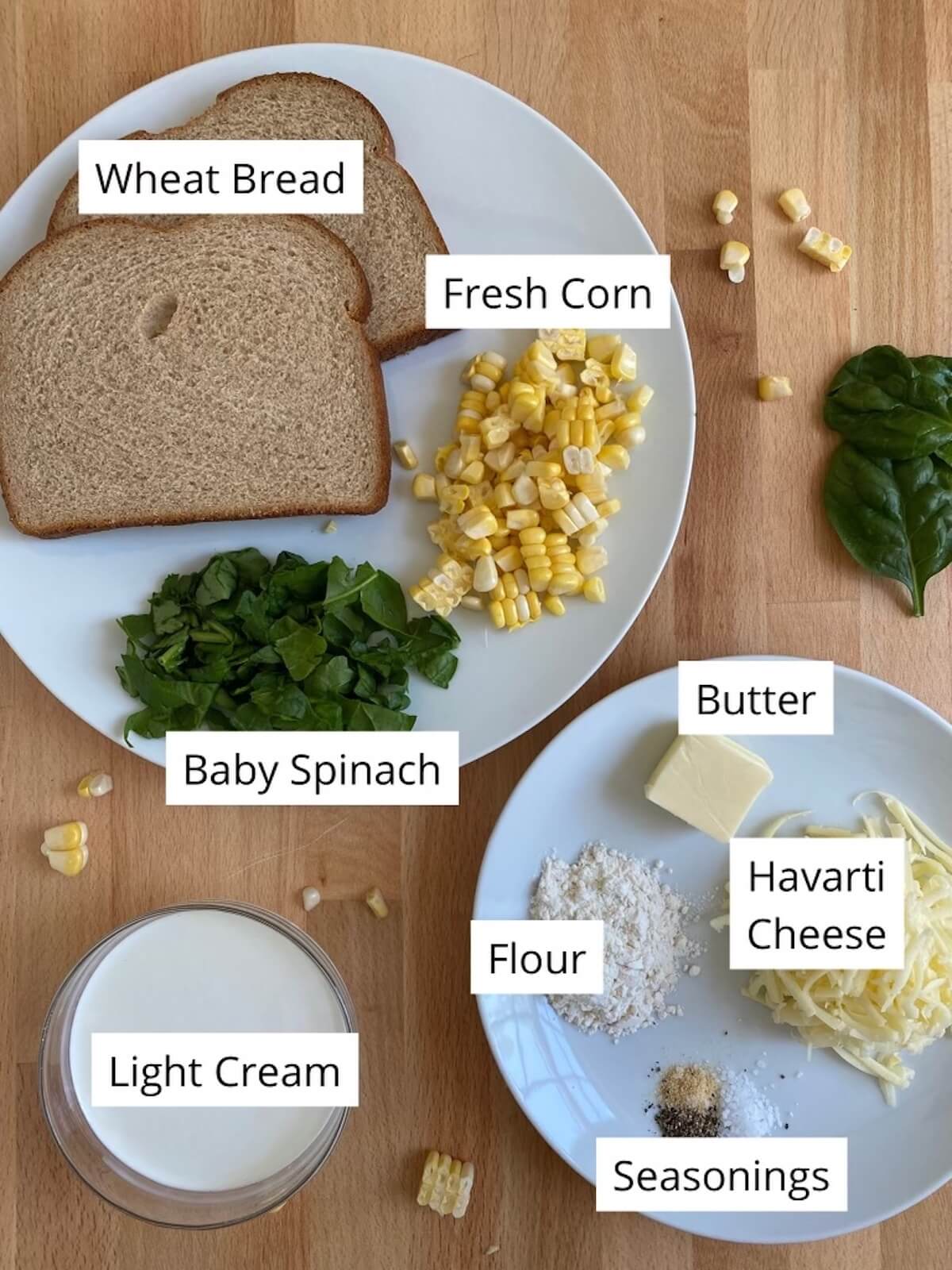 The ingredients to make a spinach corn sandwich being displayed on various white plates.