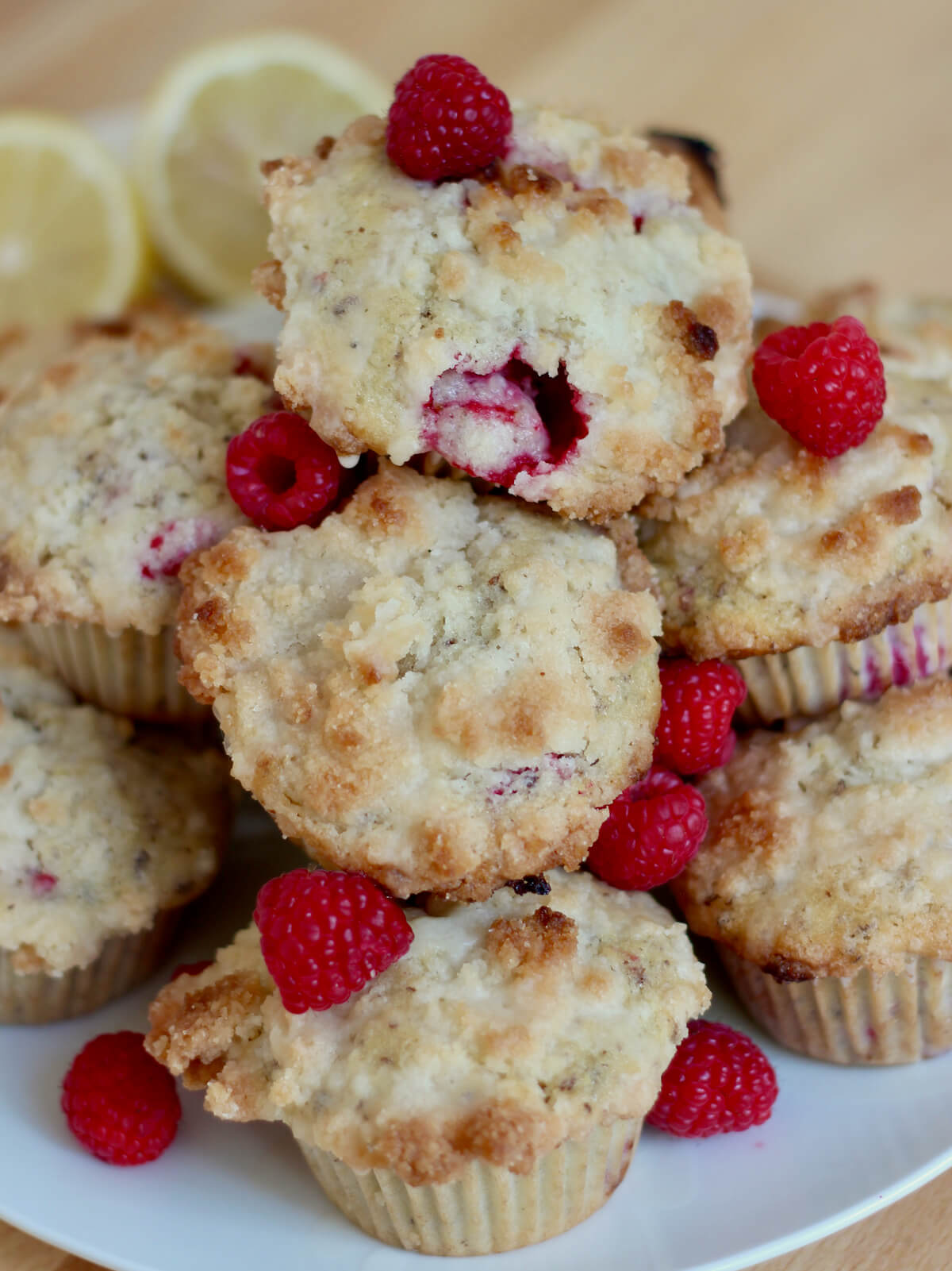 A pile of vegan raspberry muffins garnished with fresh raspberries on a white plate.