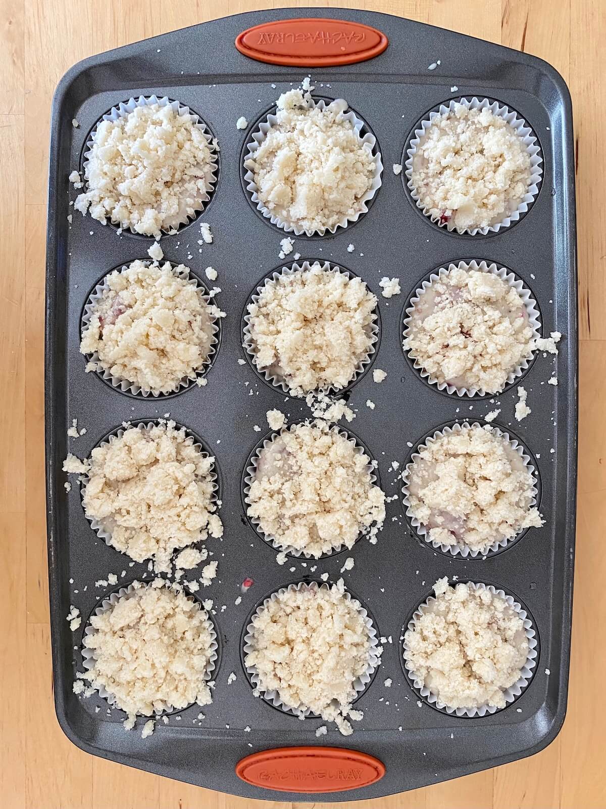 A 12-cup muffin tin filled with vegan raspberry muffin batter. Each muffin well is topped with streusel crumble.