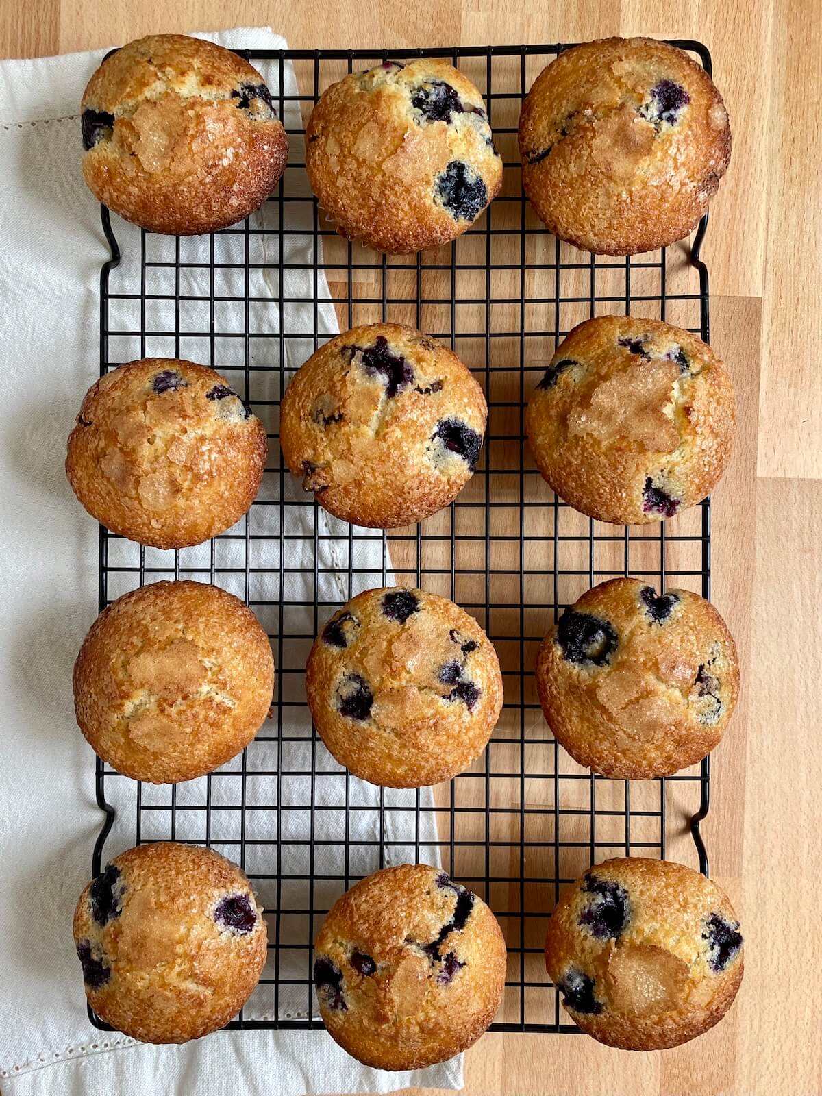 Baked blueberry chocolate chip muffins cooling on a wire rack. Beneath the rack is a white cloth napkin.