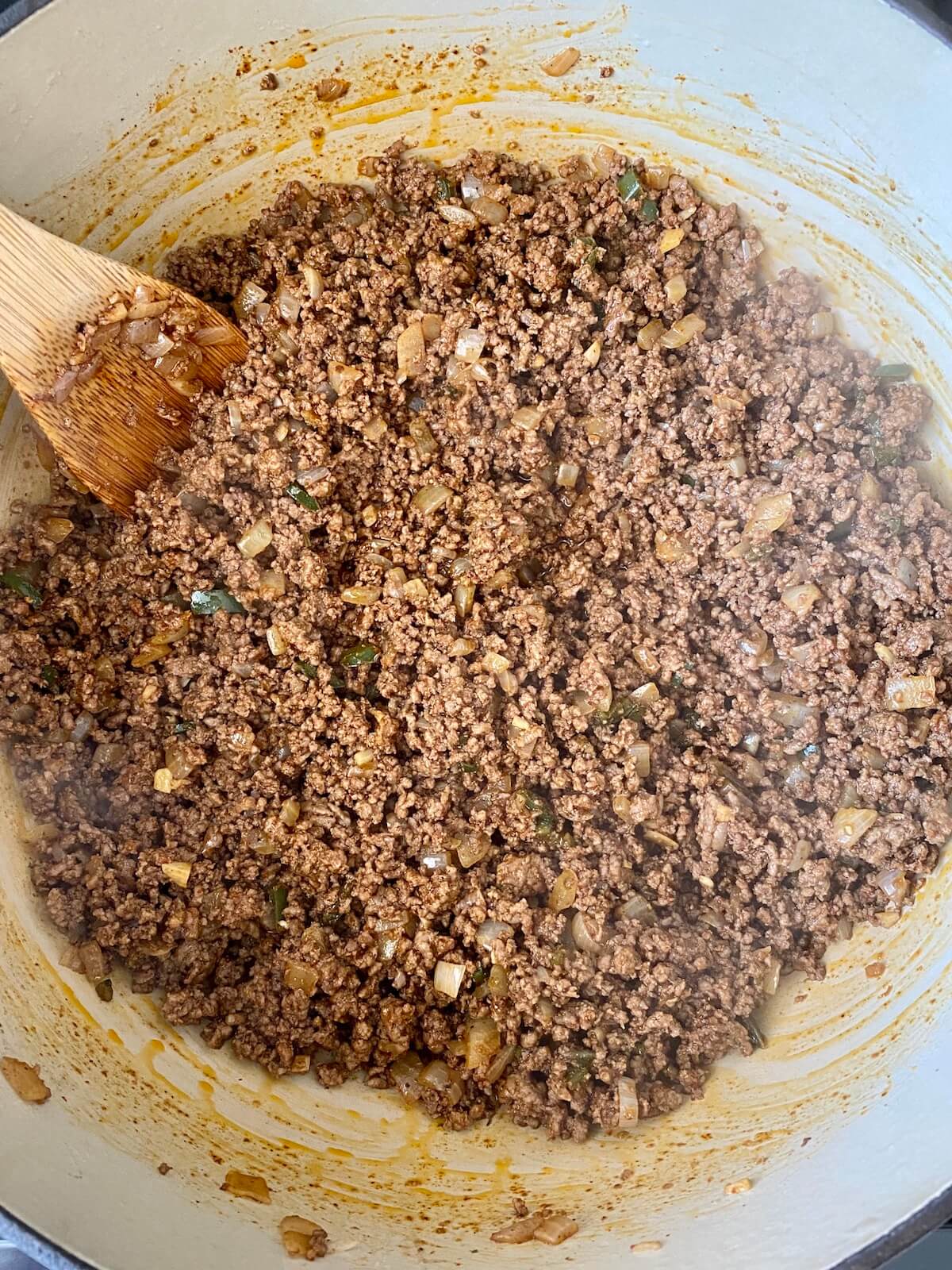 Cooked ground beef seasoned with chili powder, cumin, and cayenne pepper being sautéed in a dutch oven.