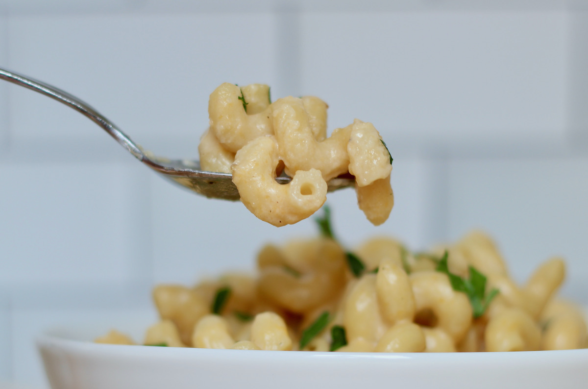 A spoonful of macaroni and cheese being held above a bowlful of macaroni and cheese.