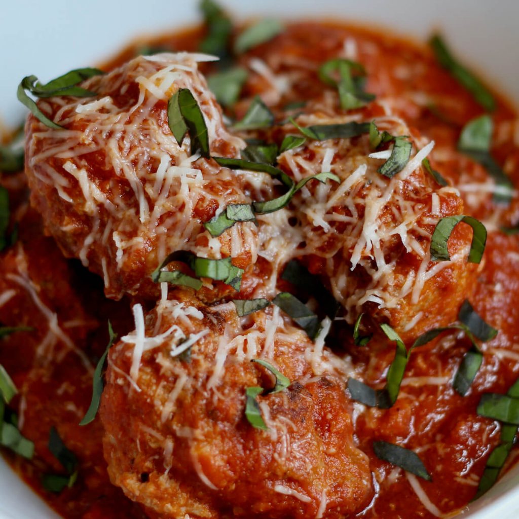 Dutch oven meatballs in tomato sauce garnished with freshly grated parmesan cheese and fresh basil.