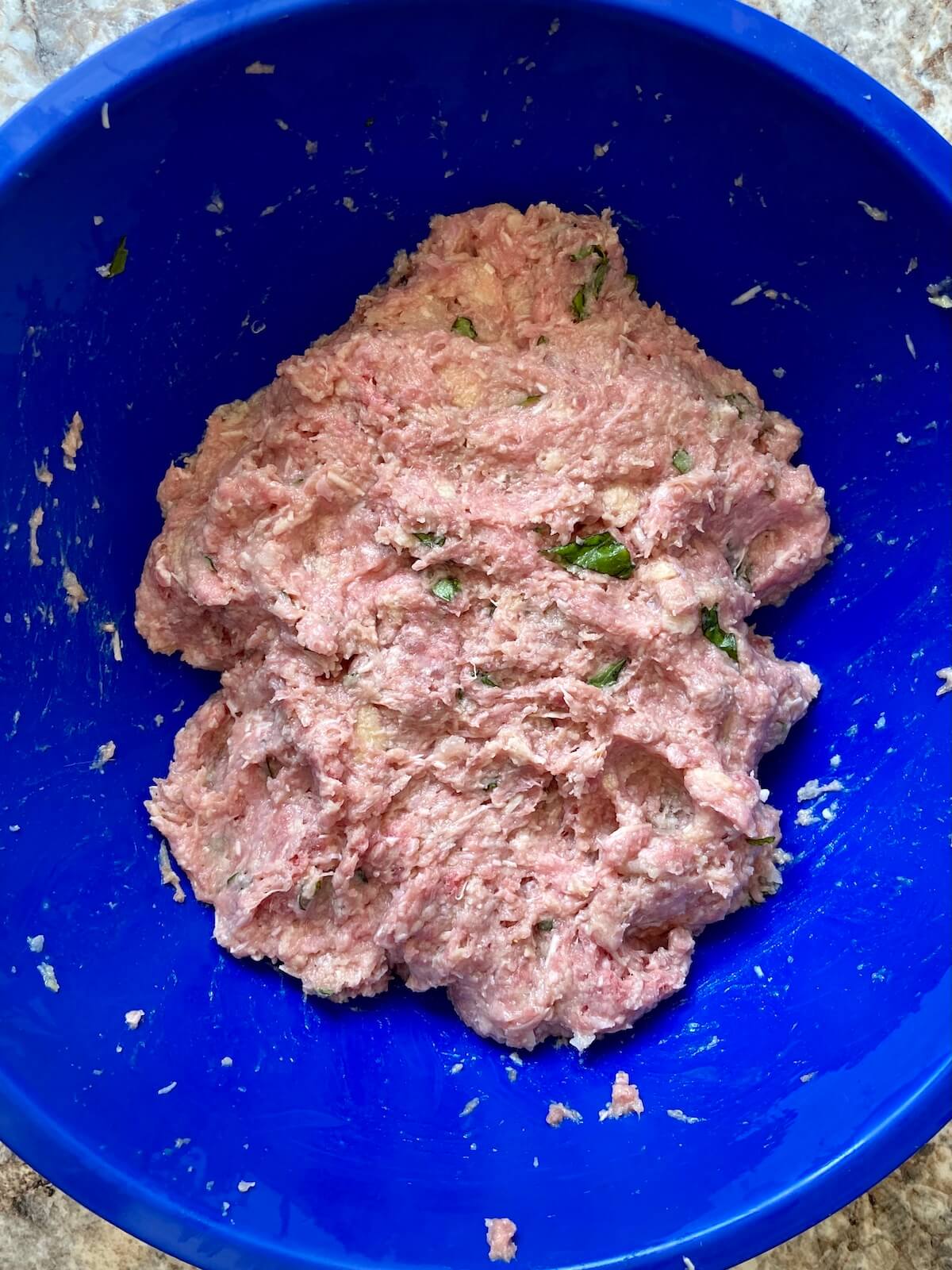 Raw meatball mixture in a royal blue mixing bowl.