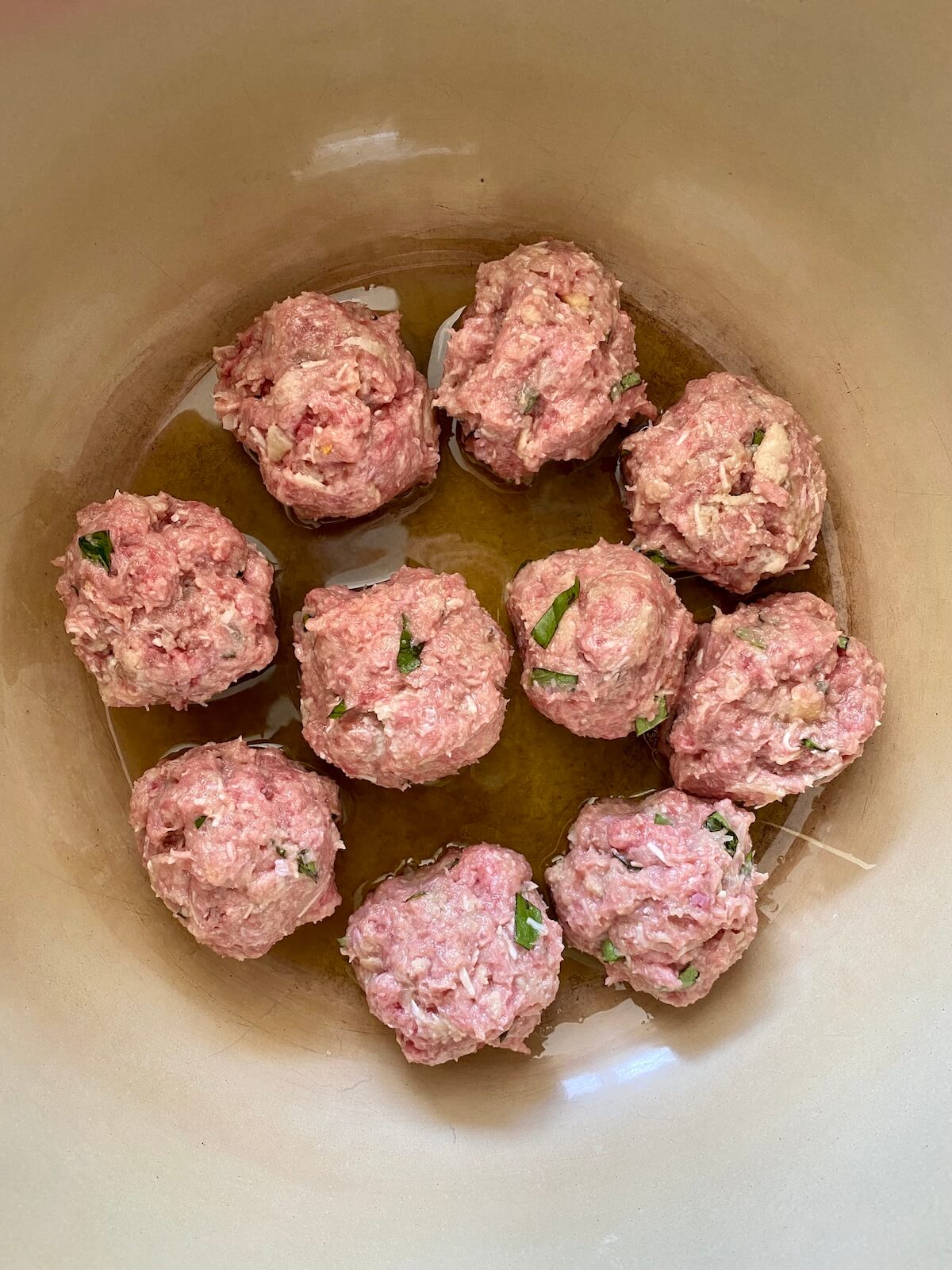 Raw meatballs being seared in olive oil in a dutch oven.
