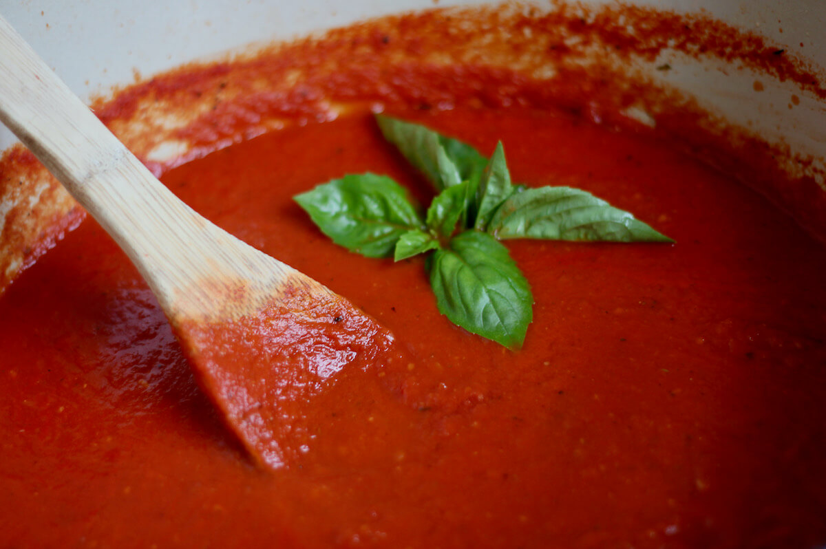 San Marzano tomato sauce garnished with fresh basil leaves. There is a wooden spoon sticking out of the pot of sauce to the left.