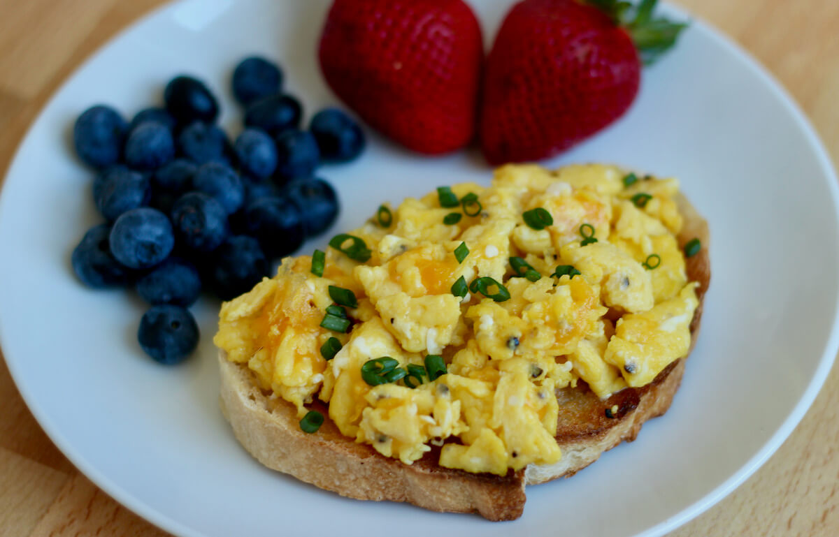 Egg toast on a small, white plate along with two strawberries and a small handful of blueberries.