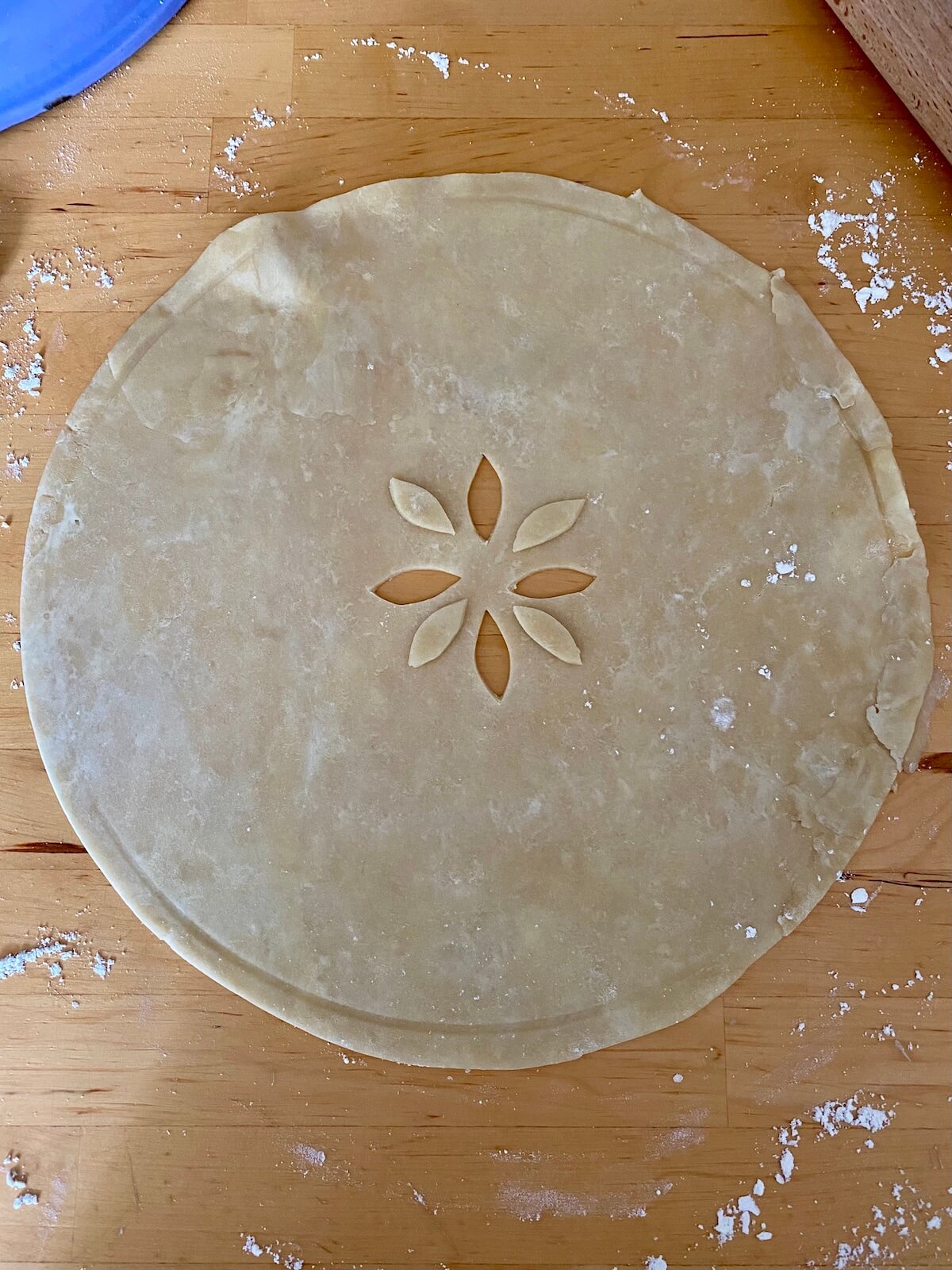A rolled out circular pie dough on a butcher block countertop. In the center of the dough, there are four little diamond shapes cut out.