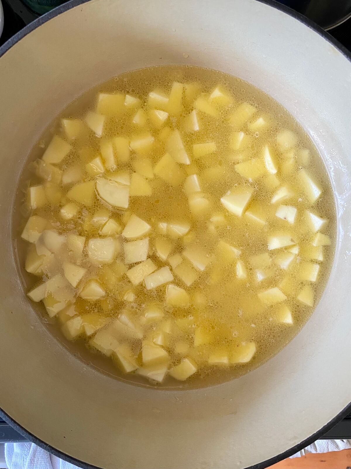 Cubed potatoes being simmered in buttery water in a large dutch oven.