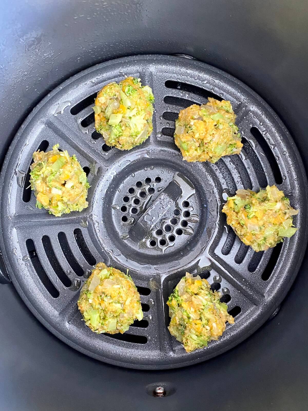 Six uncooked broccoli bites in the base of an air fryer basket.
