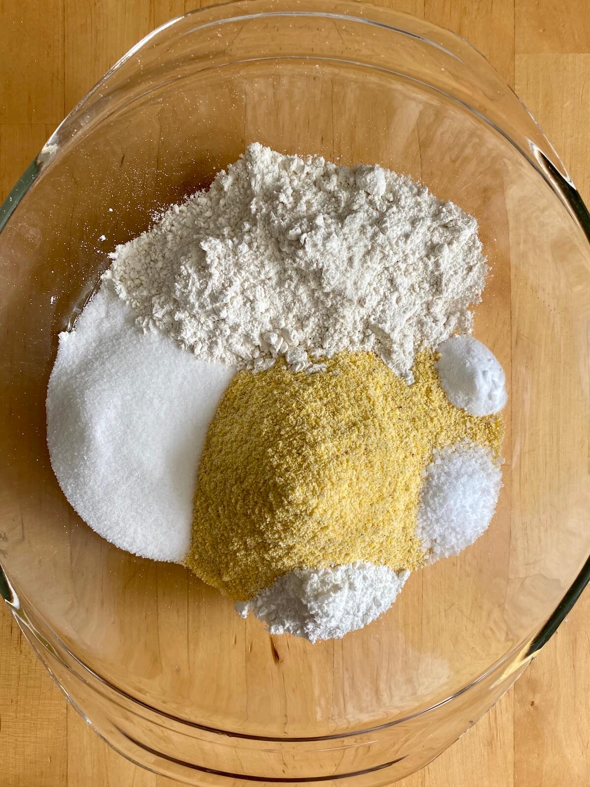 The dry ingredients used to make cornbread in a cast iron skillet in a clear glass mixing bowl. The ingredients are not yet mixed so they're easy to distinguish from one another.