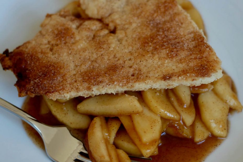 A serving of deconstructed apple pie on a small white plate. There is a fork on the plate with a few pieces of apple on it, as if someone is about to take a bite.