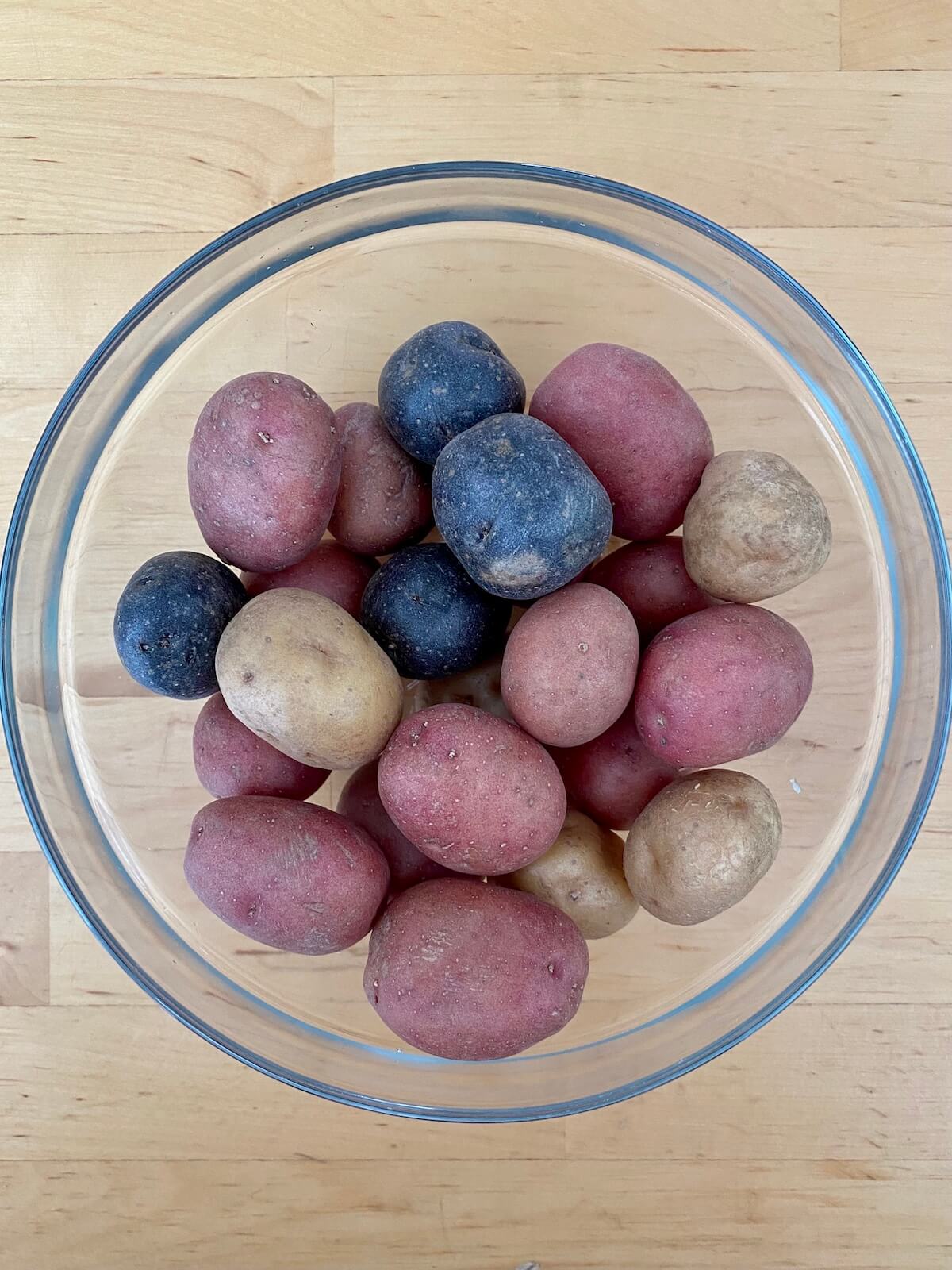 Purple, red, and white baby potatoes in a clear glass bowl.