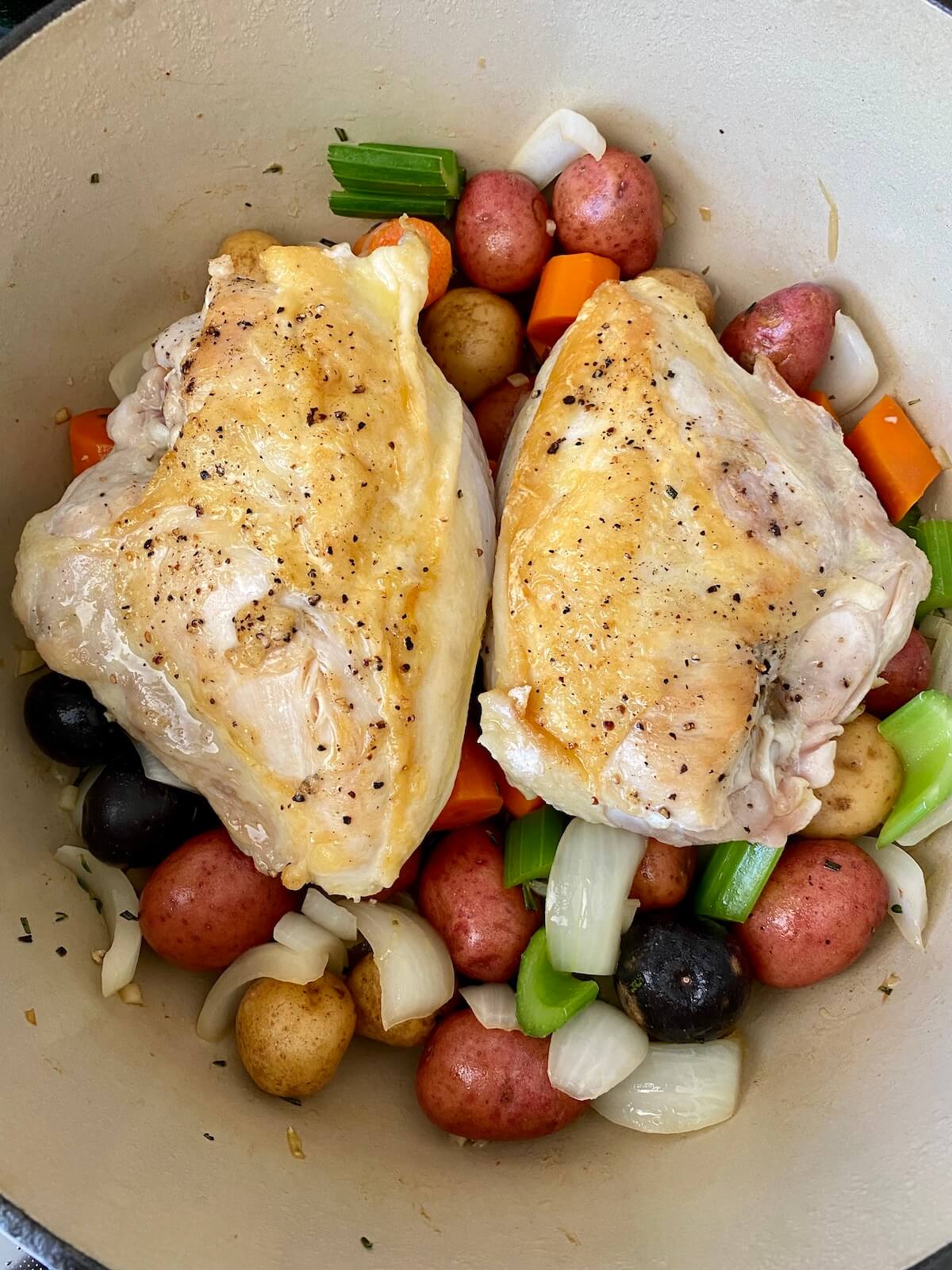 Seasoned and seared chicken breast sitting on top of vegetables in the bottom of a dutch oven.