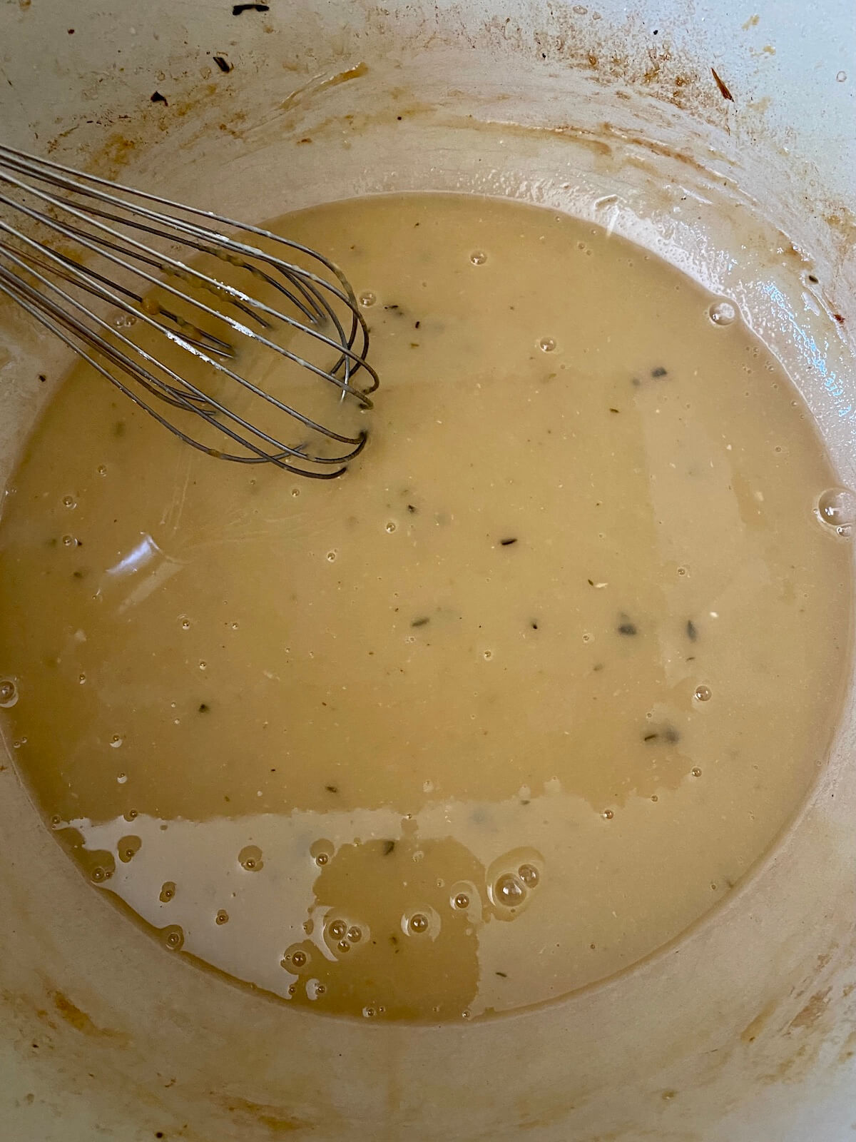 Chicken gravy simmering on the stovetop in a dutch oven. There is a whisk sticking out of the pot to the left.