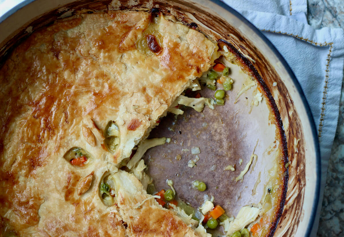 A dutch oven chicken pot pie with a large slice taken out of the pot.