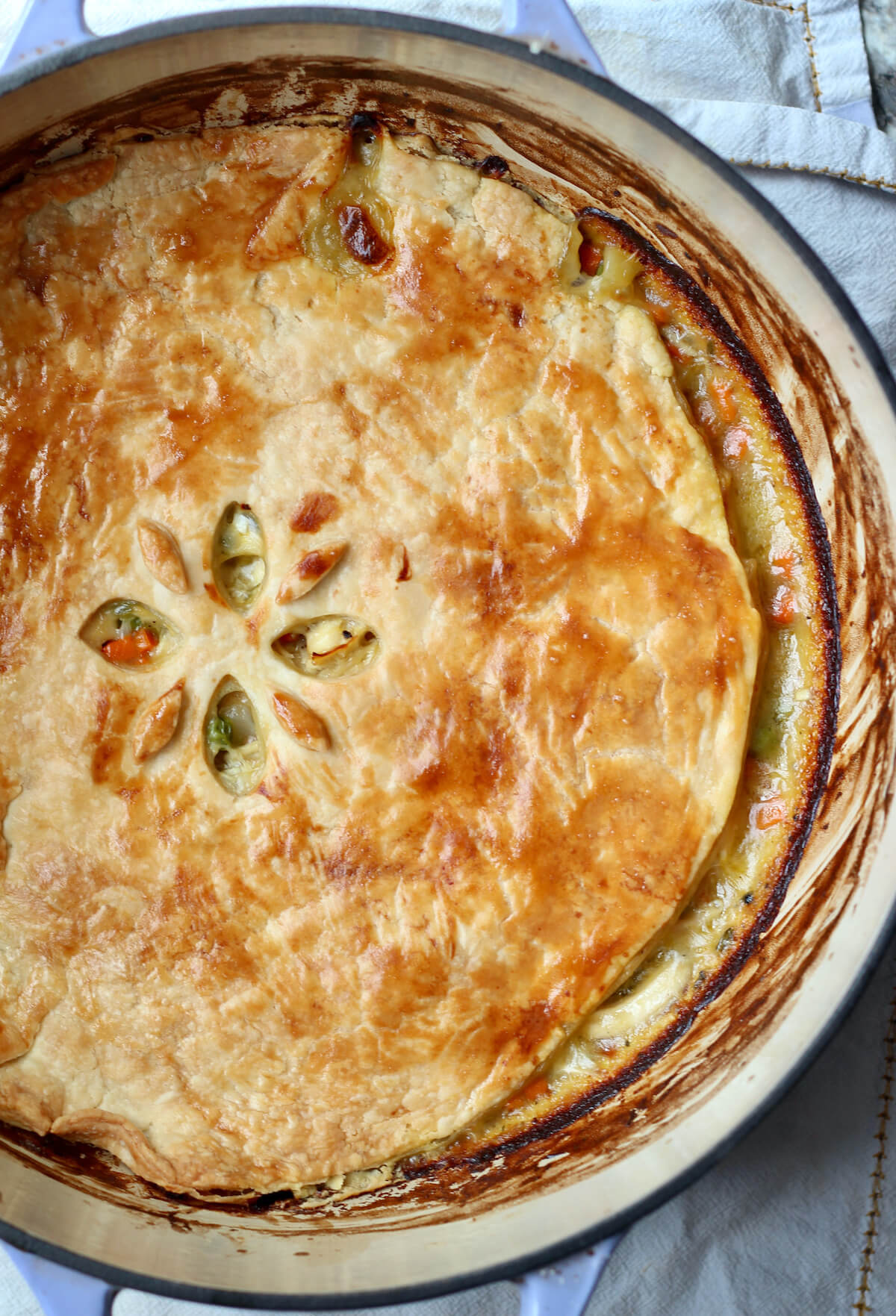A finished dutch oven chicken pot pie sits on top of a white towel on the counter.