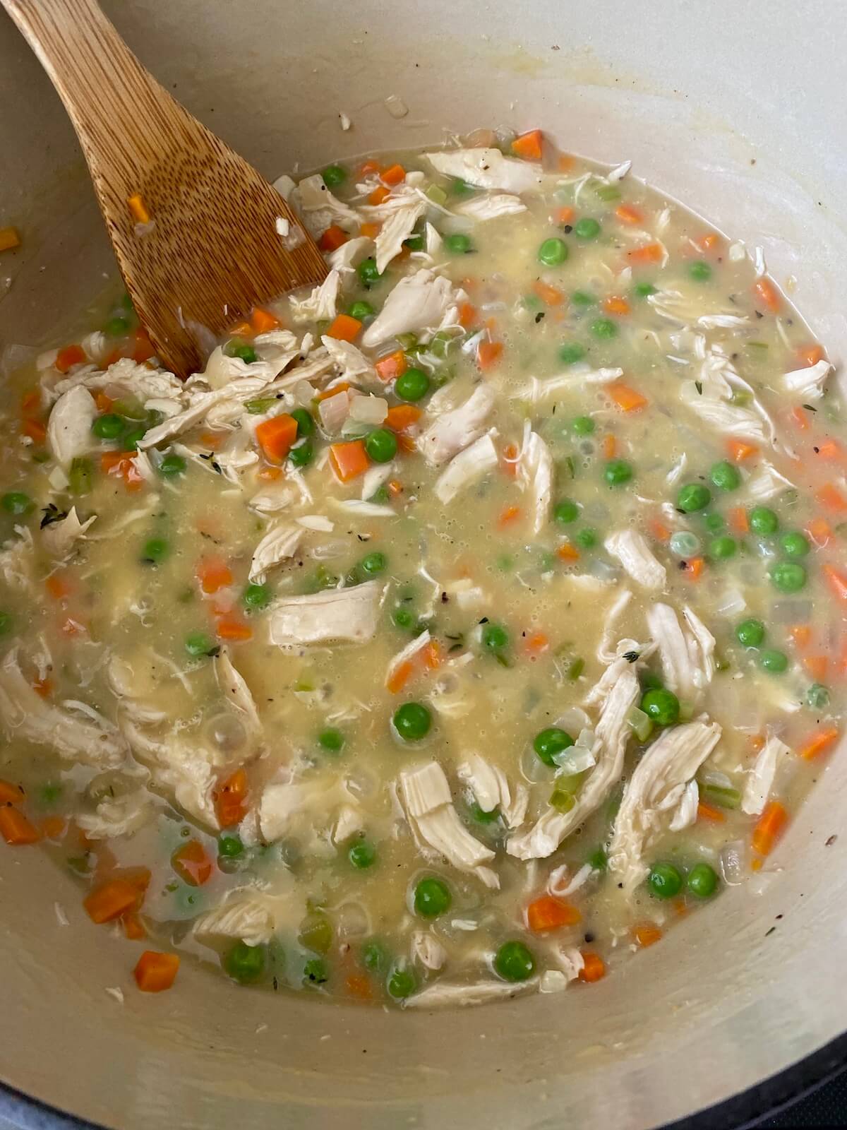 The finished chicken pot pie filling inside a dutch oven pot. There is a wooden spoon sticking out of the pot to the left.