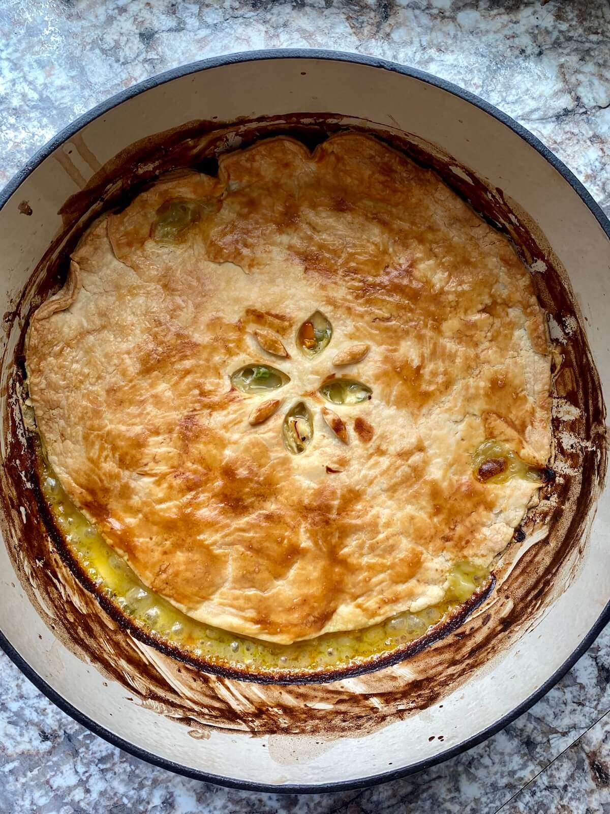 The finished dutch oven chicken pot pie. The crust is golden brown and the filling is bubbling around the edges.