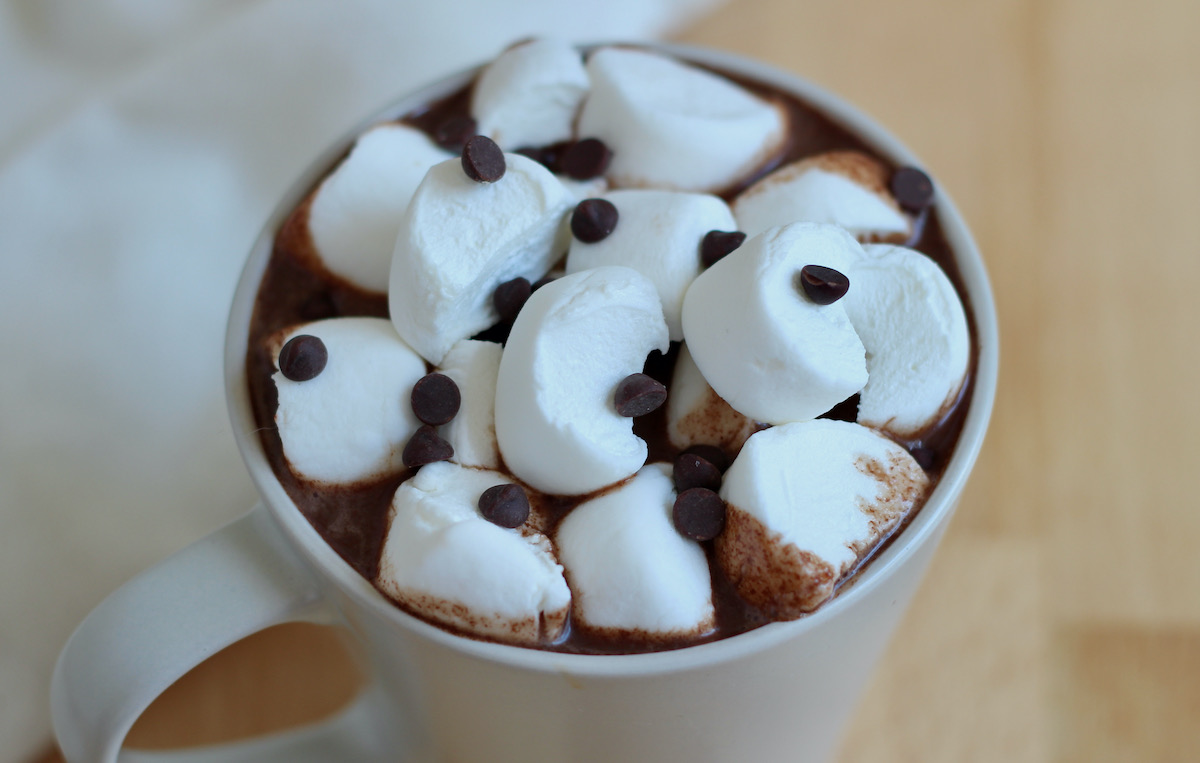 A mug of oat milk hot chocolate topped with large pieces of marshmallow and mini chocolate chips.