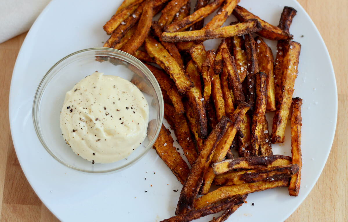 Smoky butternut squash fries on a large white plate next to garlic aioli dipping sauce.